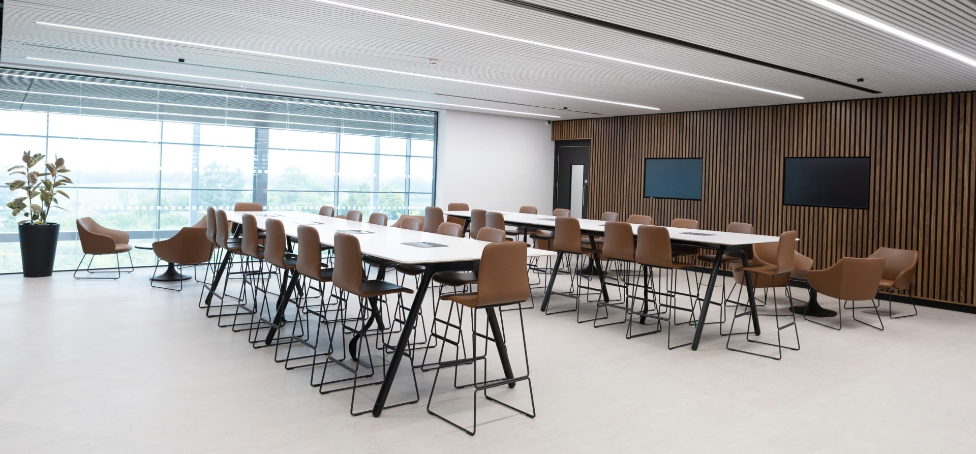 White tables and brown leather chairs with TVs on the wall and wood panels