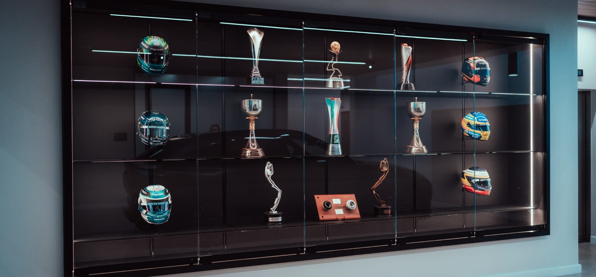 Glass trophy cabinet with helmets, trophies and memorabilia inside on a black background