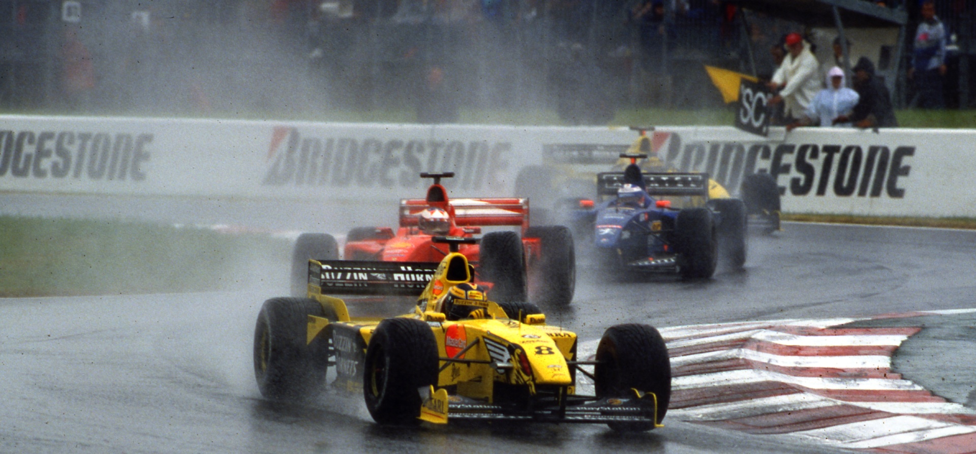 Yellow F1 car leading a red F1 car in the rain