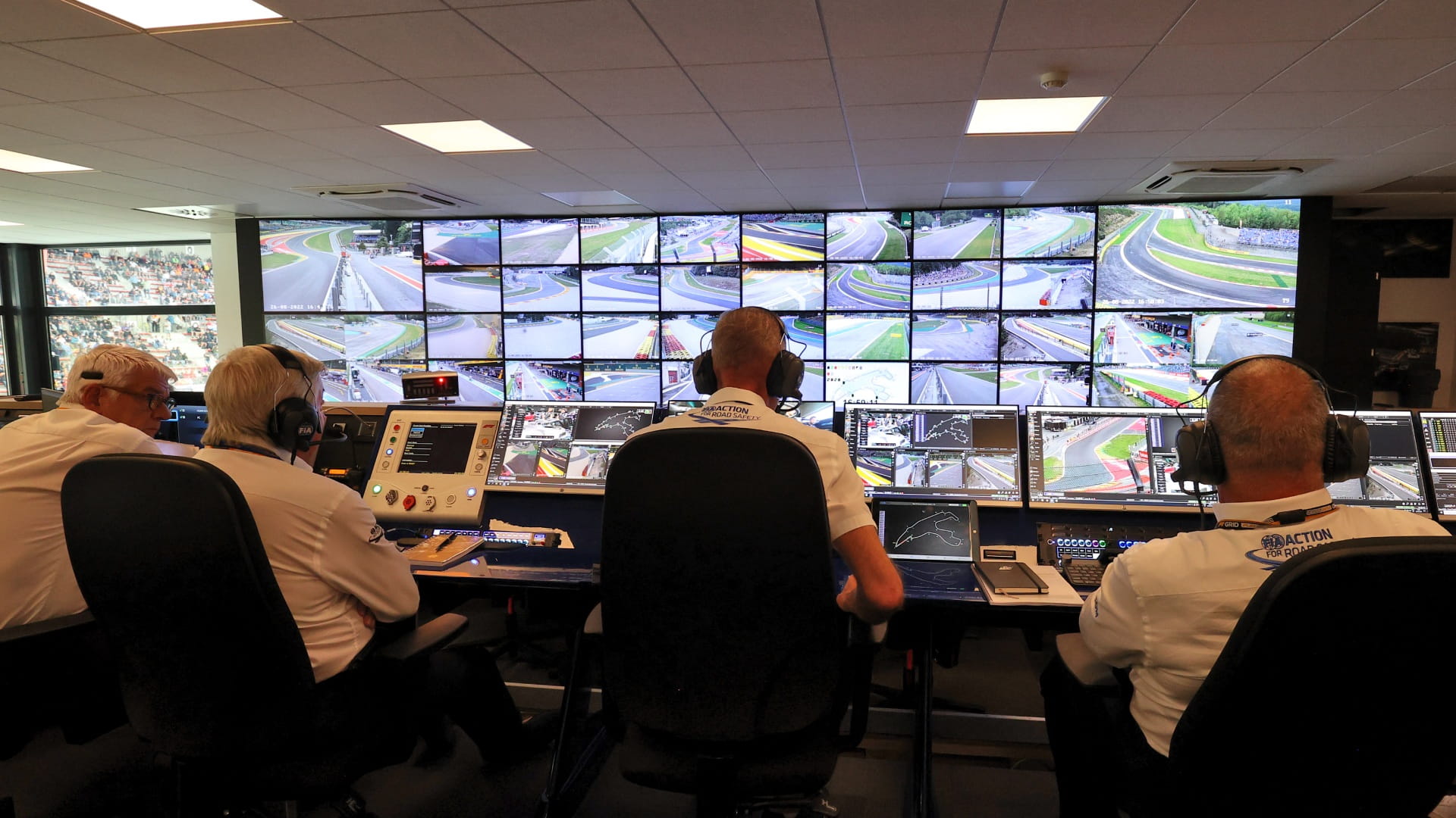 Stewards sitting in a room at an F1 race facing a bank of screens