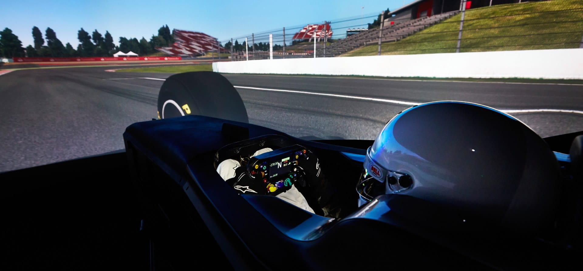 photo of an F1 simulator with  a driver wearing a white helmet watching a screen and holding a steering wheel