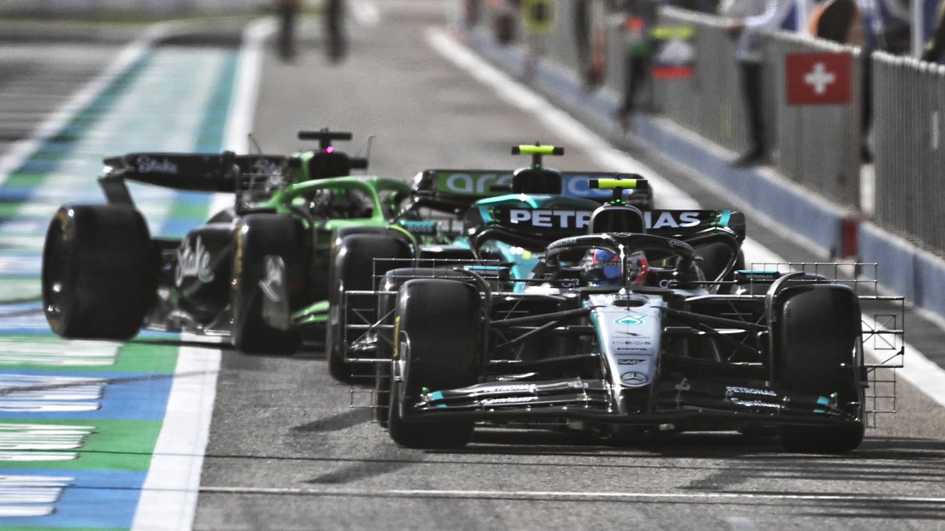 Mercedes F1 car in silver and black leading two green F1 cars in the F1 pitlane during 2025 F1 preseason testing